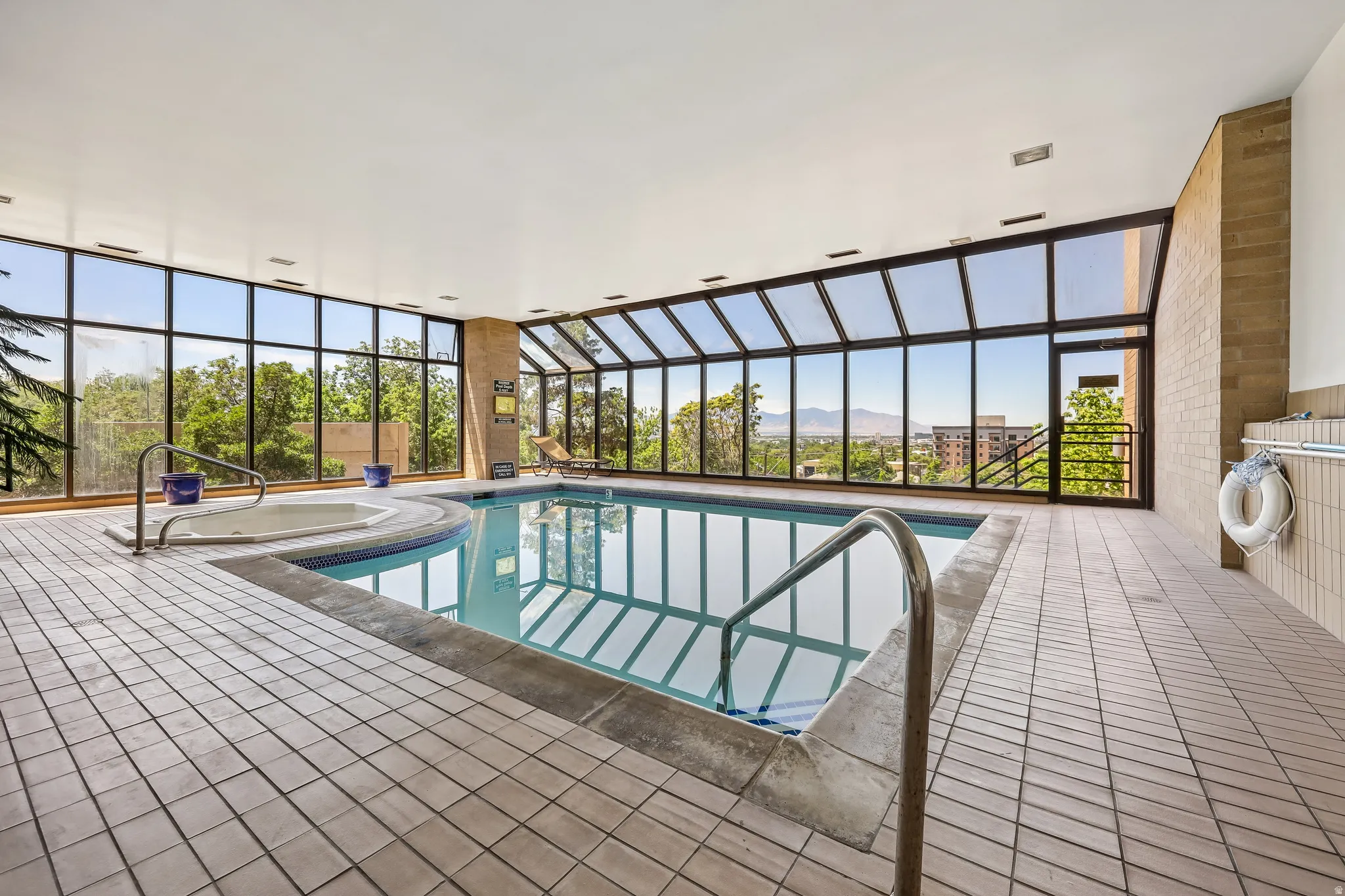 Indoor swimming pool with an integrated spa, surrounded by floor-to-ceiling windows and a tiled deck