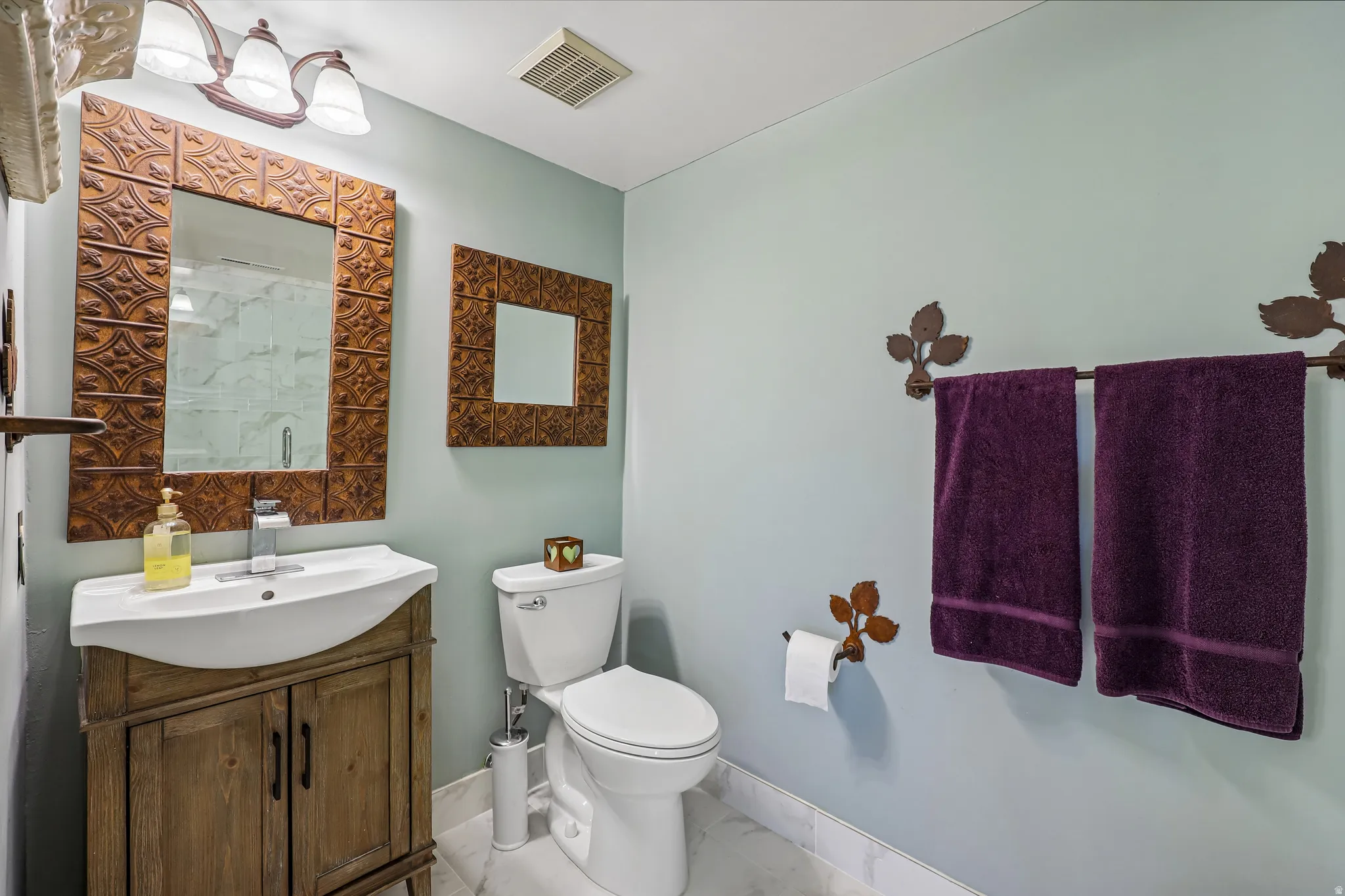 Bathroom featuring a distressed wood-finish vanity with an integrated sink, a rectangular mirror with an embossed frame, and a white toilet