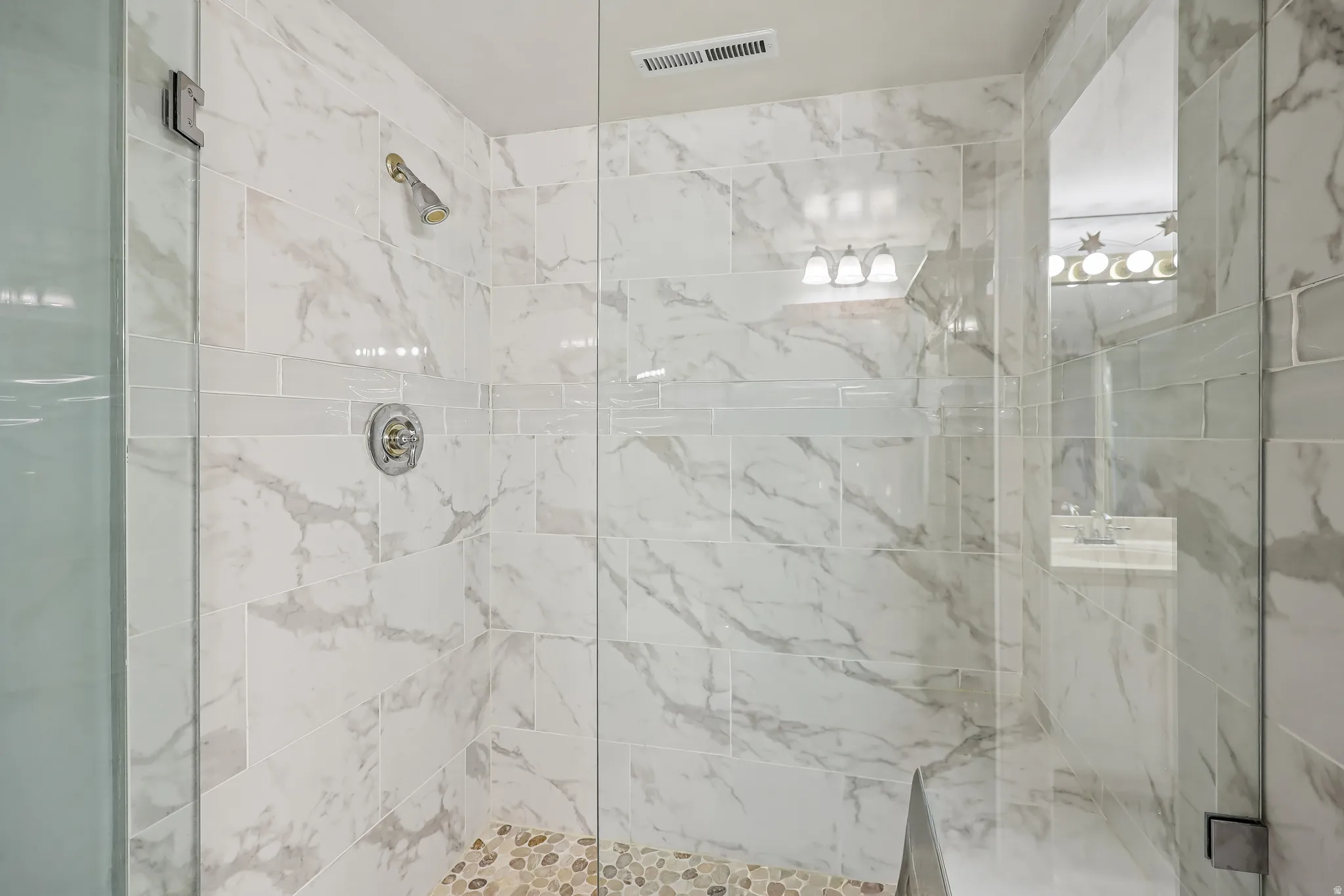 Walk-in shower featuring large format tile walls, a decorative tile accent band, and a pebble-stone floor