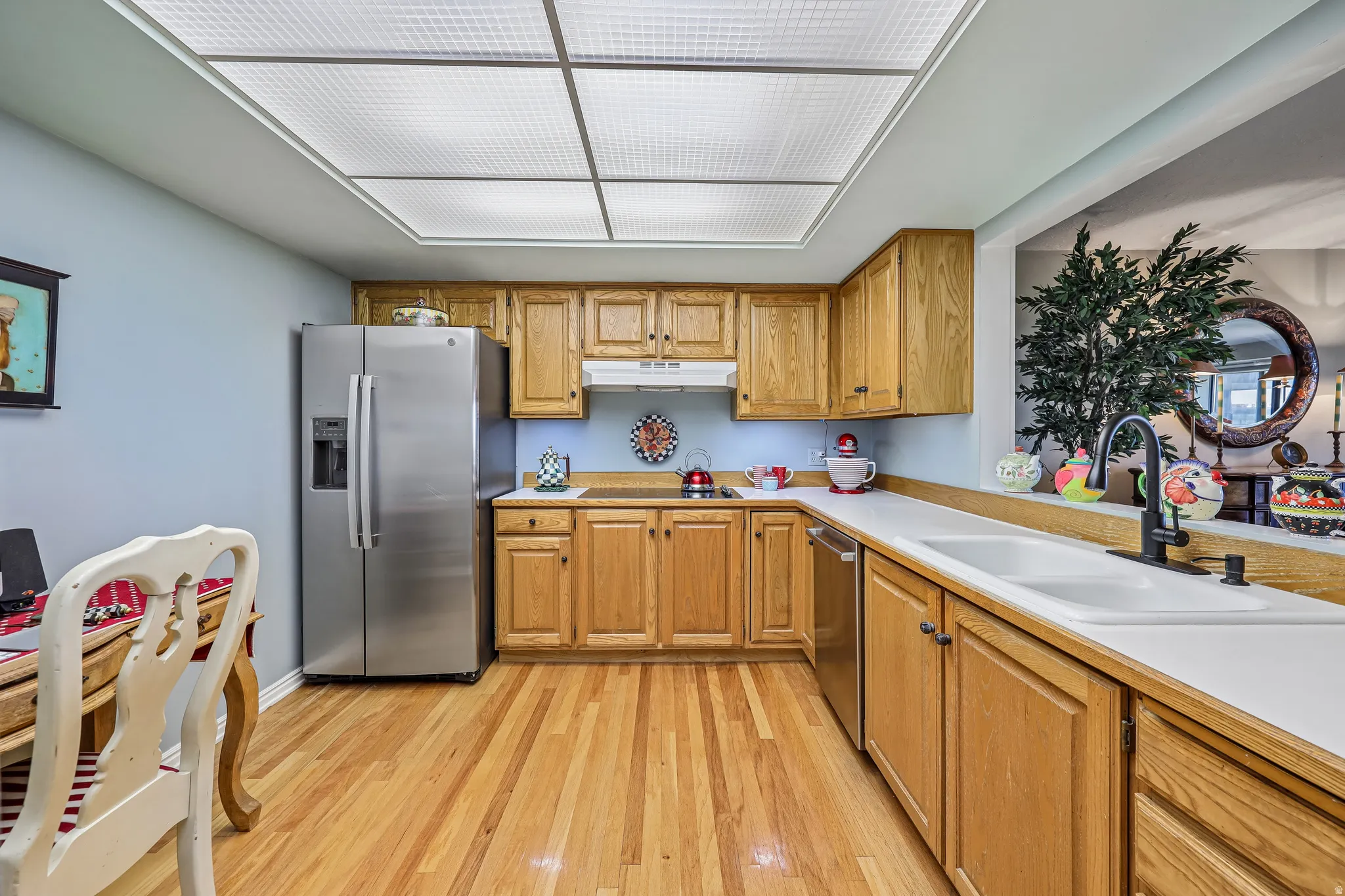 Kitchen featuring natural wood cabinetry, wood-finish flooring, stainless steel appliances, white countertops, and a double basin sink with a matte black faucet