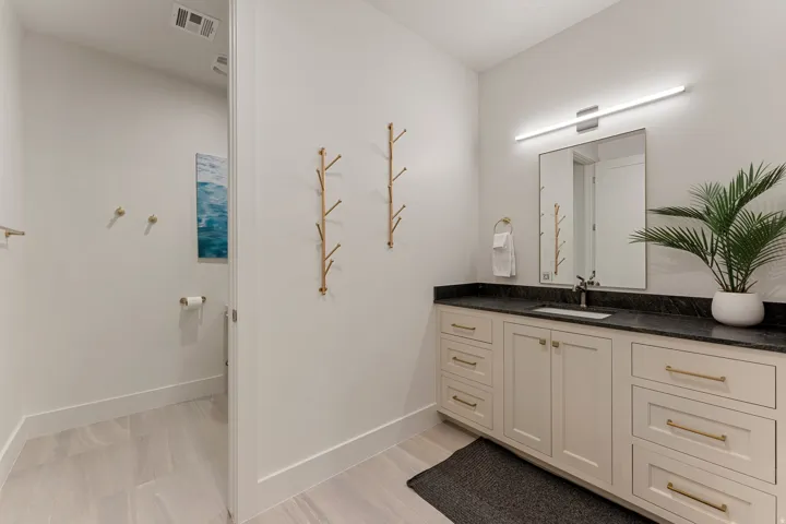 Bathroom featuring a light wood-finish floor, a long vanity with cream cabinetry, gold hardware, a dark countertop, and an undermount sink with a wall-mounted mirror