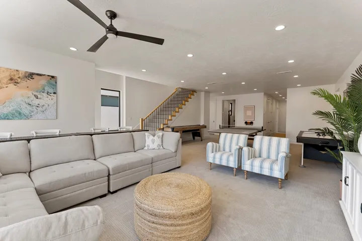 Spacious recreation room featuring recessed lighting, a modern ceiling fan, and a wood staircase with black metal balusters