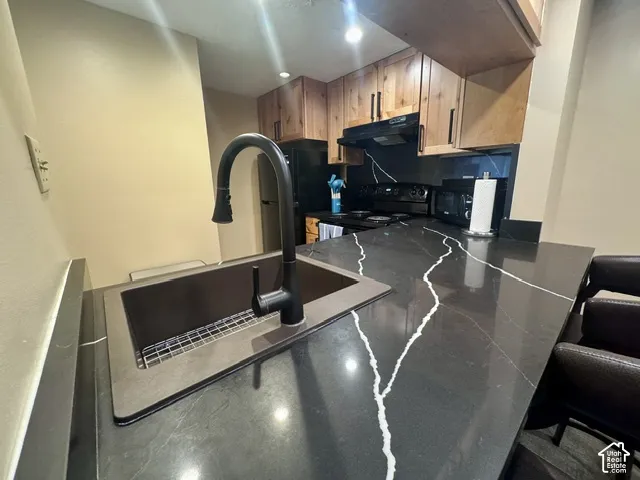 Kitchen featuring dark countertops with white veining, a matte black gooseneck faucet, an undermount sink, recessed lighting, and wood-finish cabinetry with black hardware