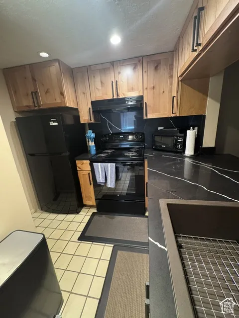Kitchen featuring black appliances, wood cabinetry, black countertops with white veining, and a large single-basin sink