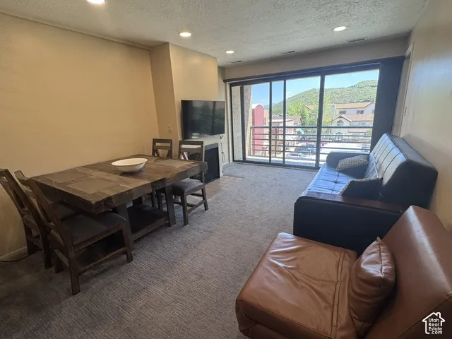 Open-concept living space featuring a sliding glass door to the exterior, recessed ceiling lighting, textured carpet flooring, and a built-in fireplace
