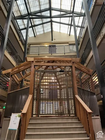 Multi-level atrium featuring a pitched glass roof, exposed metal beams, and a wood-framed elevator enclosure with metal grating