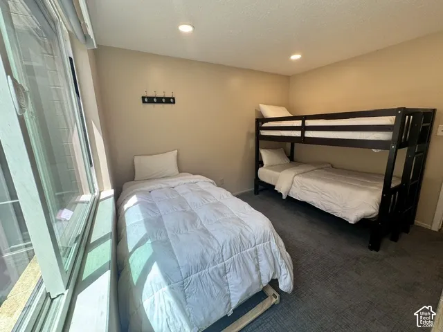Bedroom featuring a large window, recessed lighting, wall-mounted coat rack, light-toned walls, and dark-toned carpeting