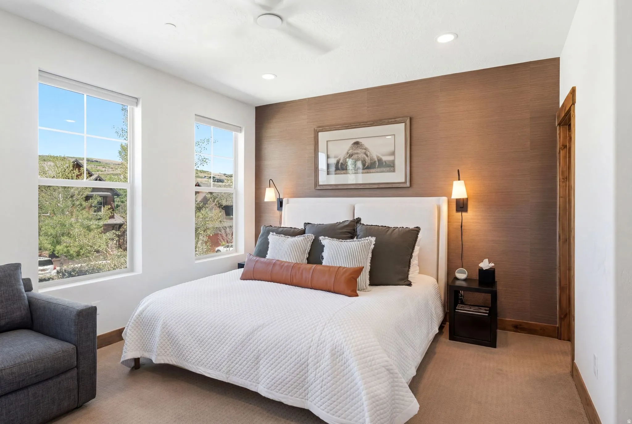 Bedroom featuring a textured accent wall, two large windows, a ceiling fan with integrated lighting, recessed lighting, and wall-mounted sconces