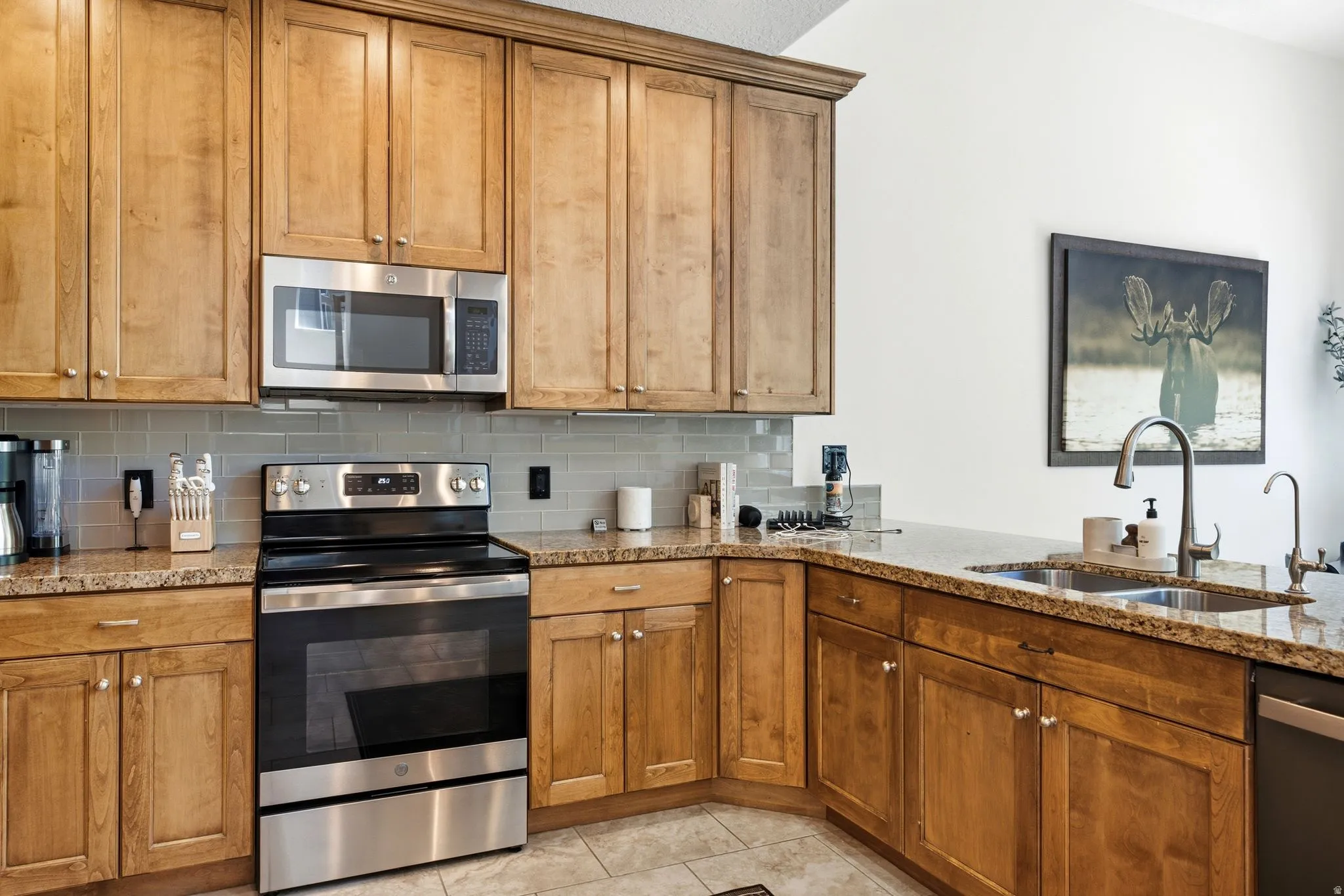 Kitchen featuring wood cabinetry, light-toned countertops, a stainless steel microwave, a stainless steel range, and a dual-basin sink with a gooseneck faucet