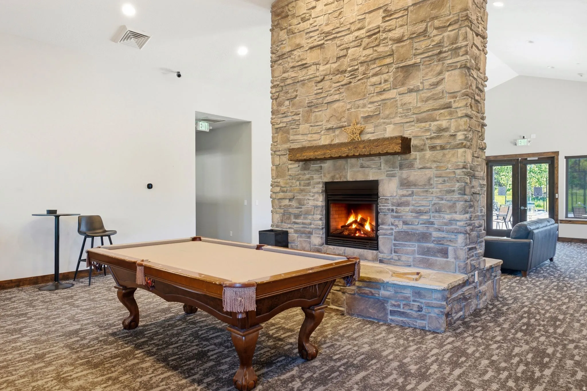 Expansive room featuring a stone fireplace with a wood mantle, vaulted ceilings, recessed lighting, and double glass doors