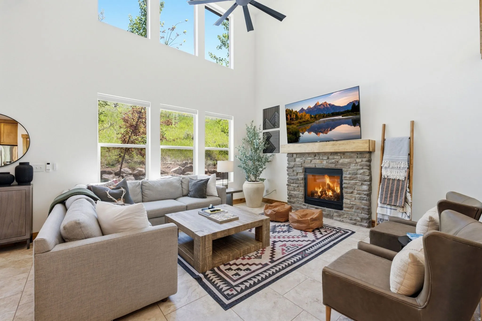 Spacious living area featuring a stone fireplace with a wood mantel, vaulted ceilings, and large windows