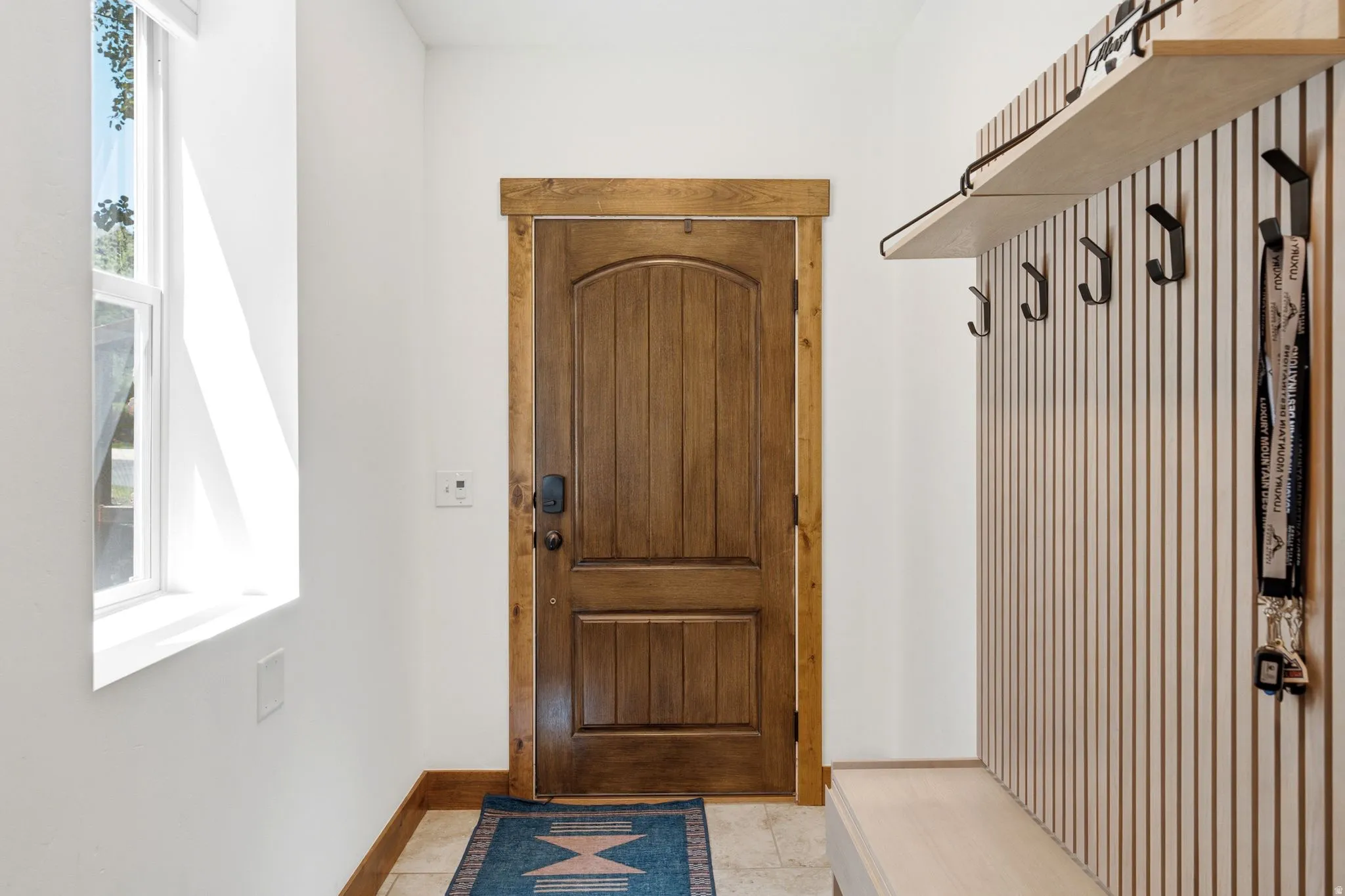 Entryway featuring a paneled wood door with a dark finish, wood-trim door casing, and a light wood-finish built-in bench with integrated hooks and a shelf
