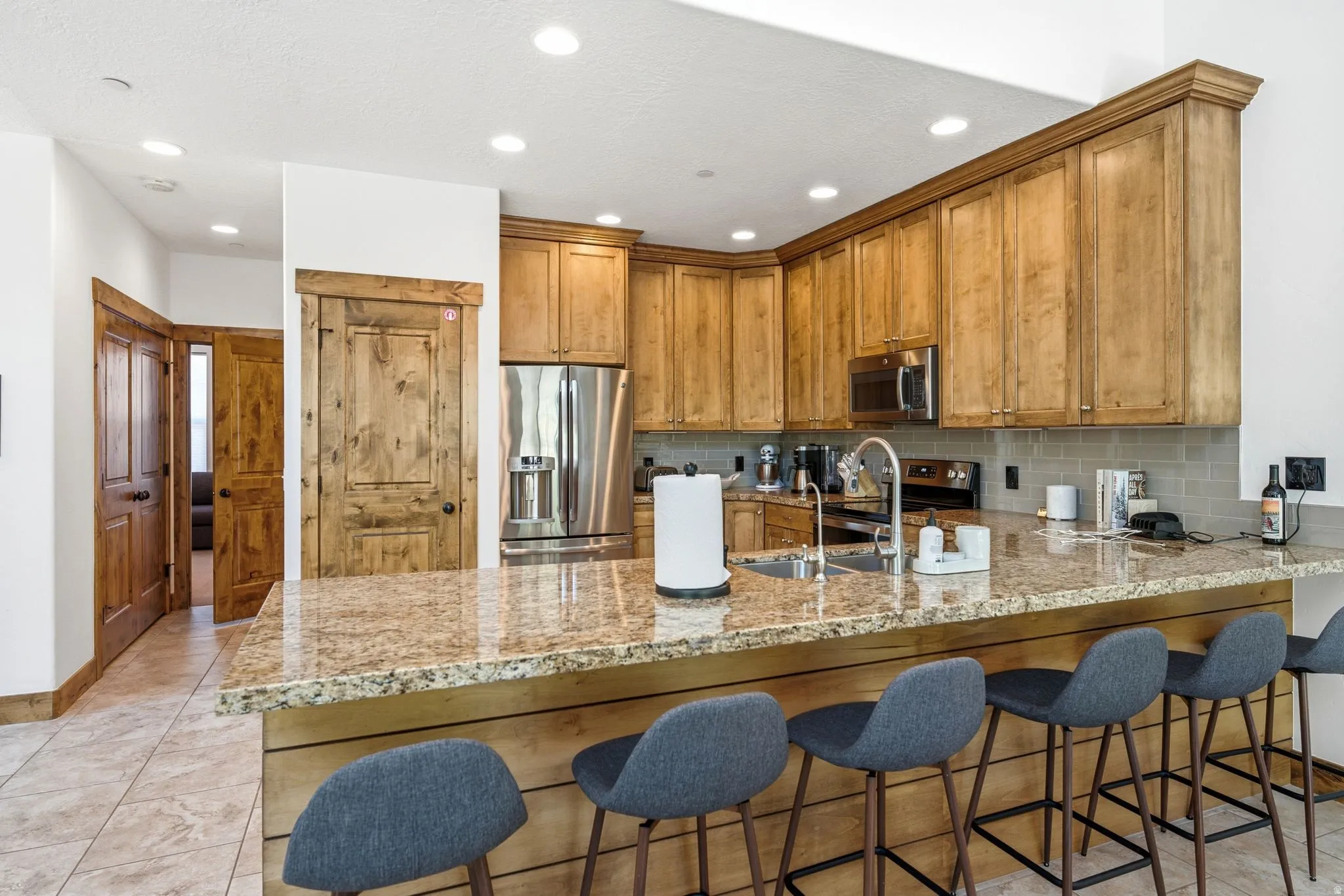 Kitchen featuring a large breakfast bar with stone countertop, stainless steel appliances, wood-finish cabinetry, a subway tile backsplash, and recessed lighting