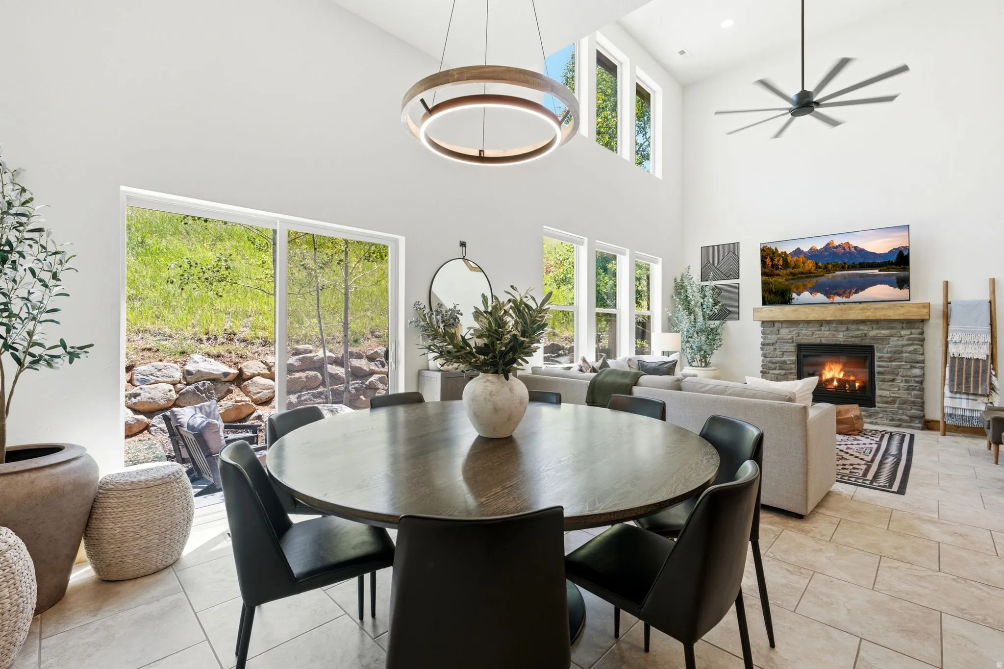 Open-concept living space featuring a stone-clad fireplace with a wood mantel, high vaulted ceilings, and large format tile flooring