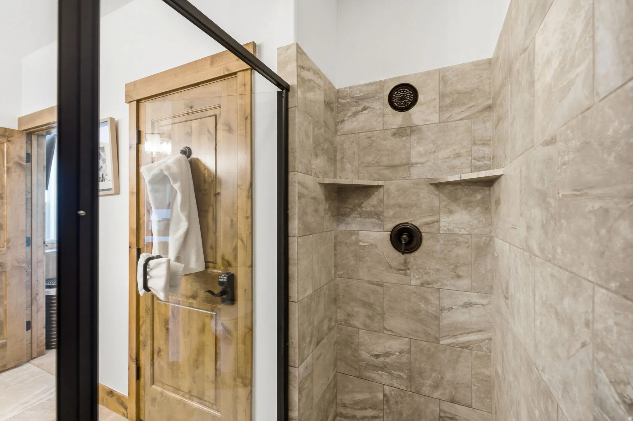 Walk-in shower featuring large format tile, dual shower niches, a bronze showerhead, and a bronze shower valve