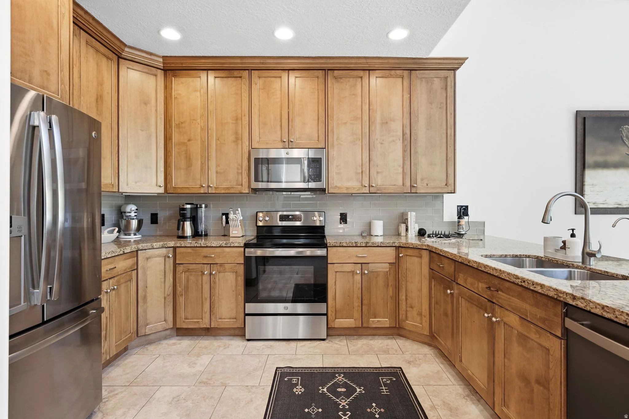 U-shaped kitchen featuring light wood cabinetry, a stainless steel appliance suite, granite countertops, a tile backsplash, and recessed lighting