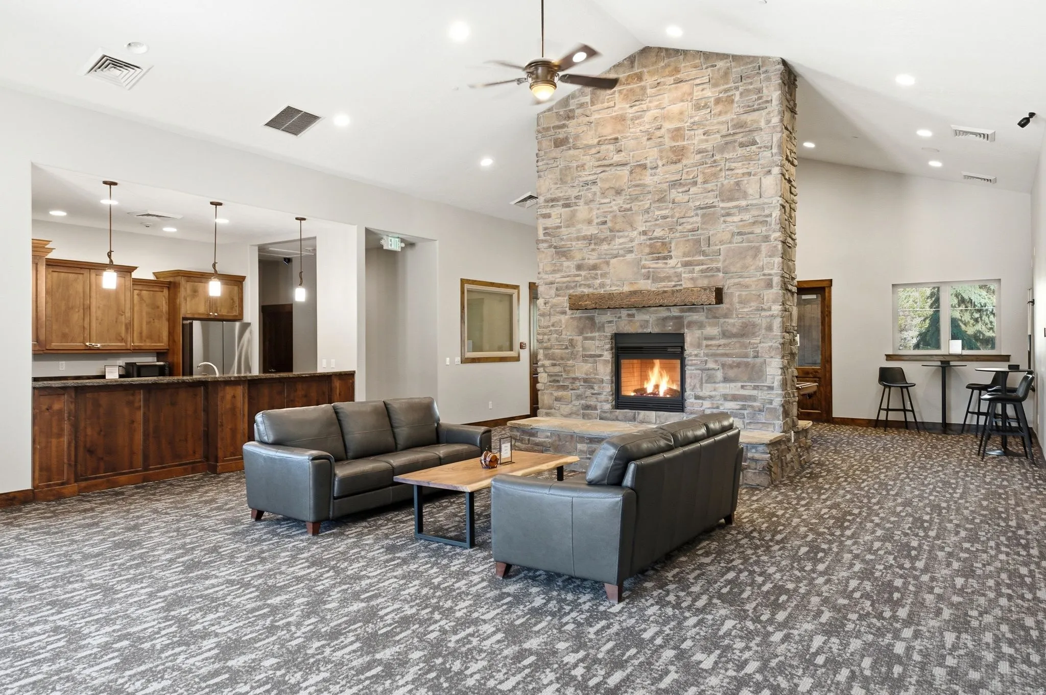 Spacious common area featuring a stone-clad fireplace with wood mantel, vaulted ceilings, and recessed lighting