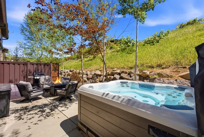 Outdoor patio featuring a built-in hot tub, a paved surface, a privacy fence, a rock retaining wall, and mature trees