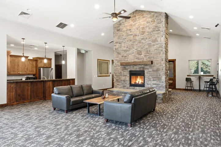 Spacious common area featuring a stone-clad fireplace with wood mantel, vaulted ceilings, and recessed lighting