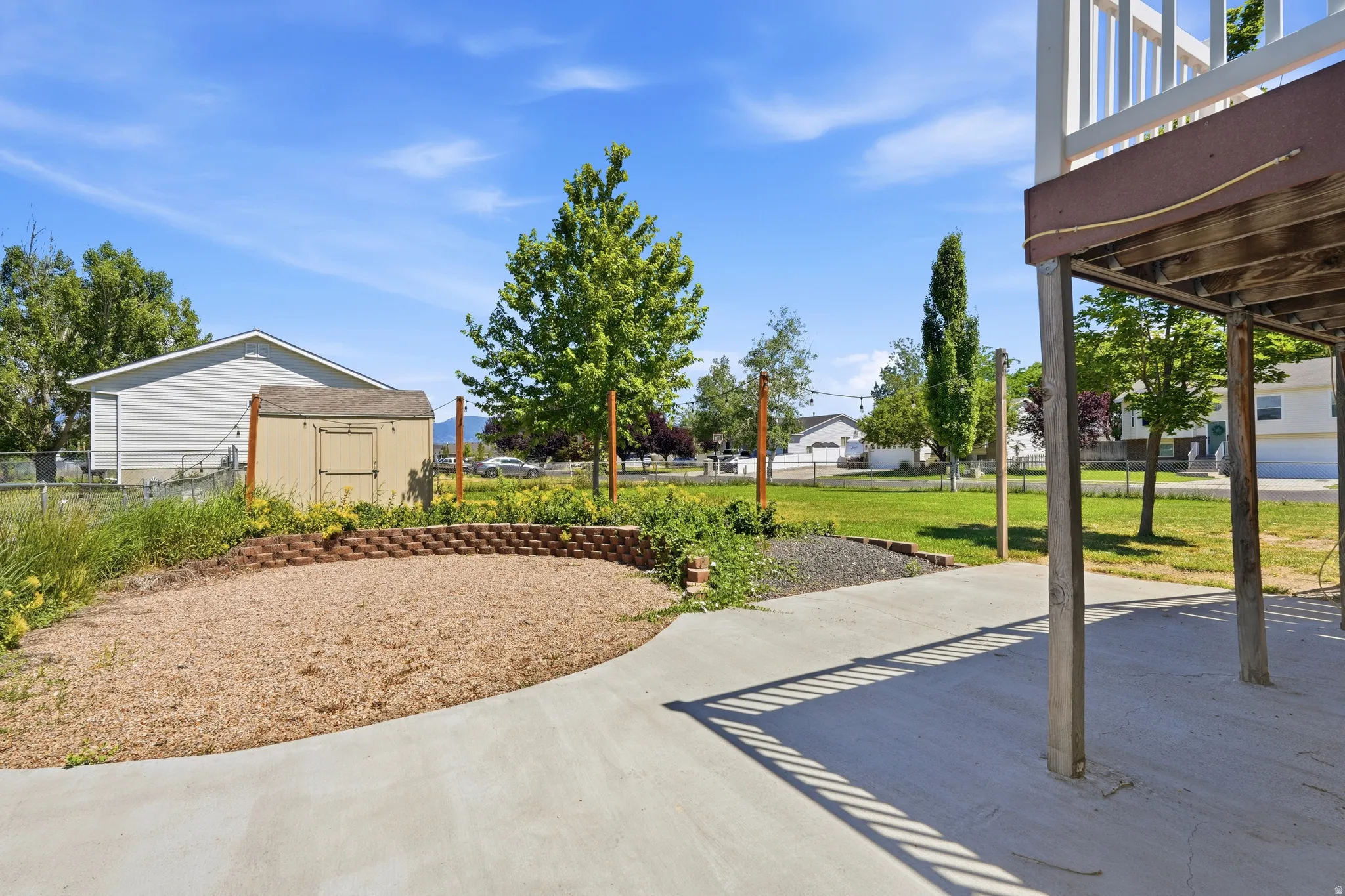Spacious backyard featuring a concrete patio, wood chip area with a brick retaining wall, and a storage shed