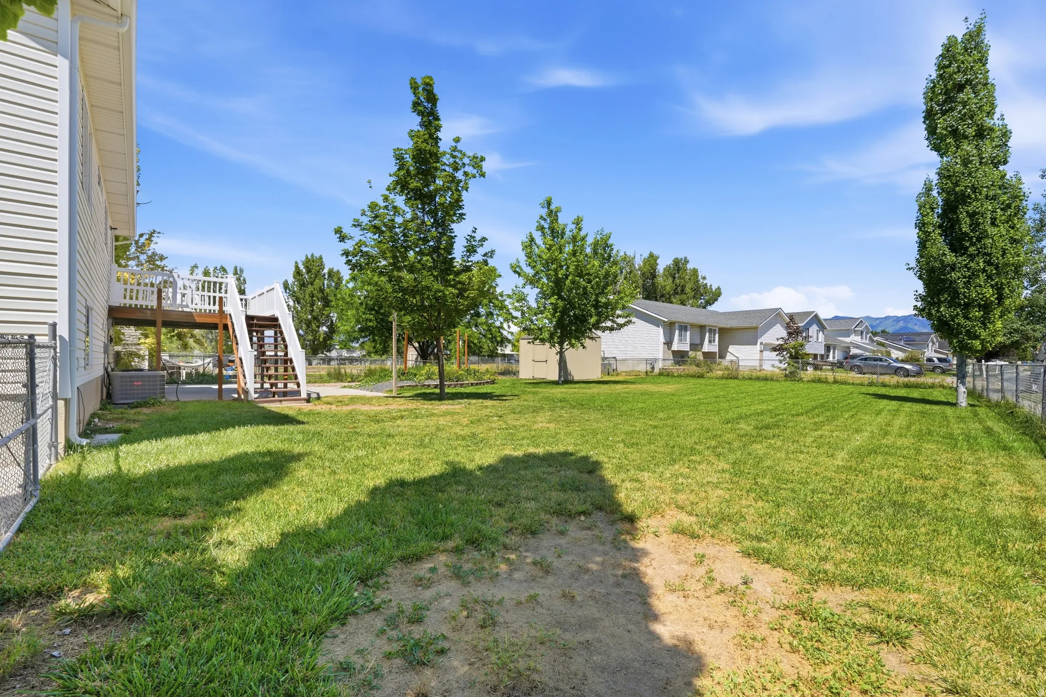 Expansive grassy yard featuring perimeter chain-link fencing, mature trees, and a multi-level deck with white railings