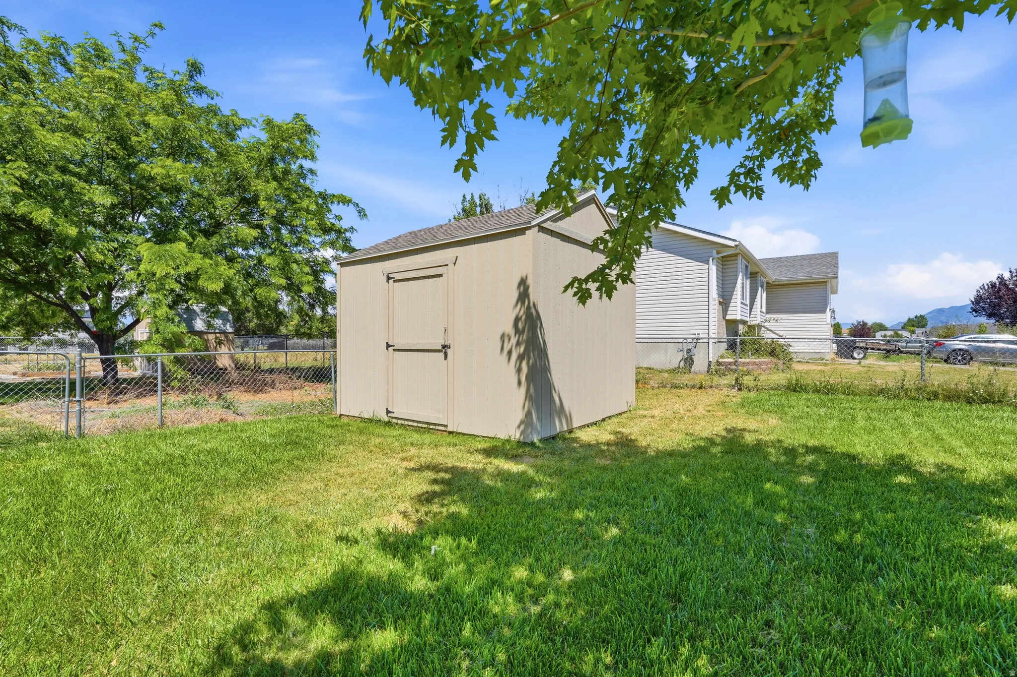 Expansive backyard featuring a detached storage shed with a dual-door entry, a chain-link fence, and mature trees providing natural shade