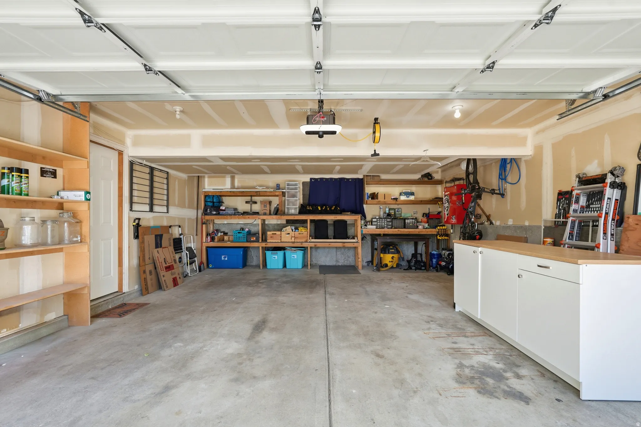 Spacious garage featuring a concrete floor, overhead garage door, built-in wooden shelving, and additional white cabinetry with a wood-finish countertop