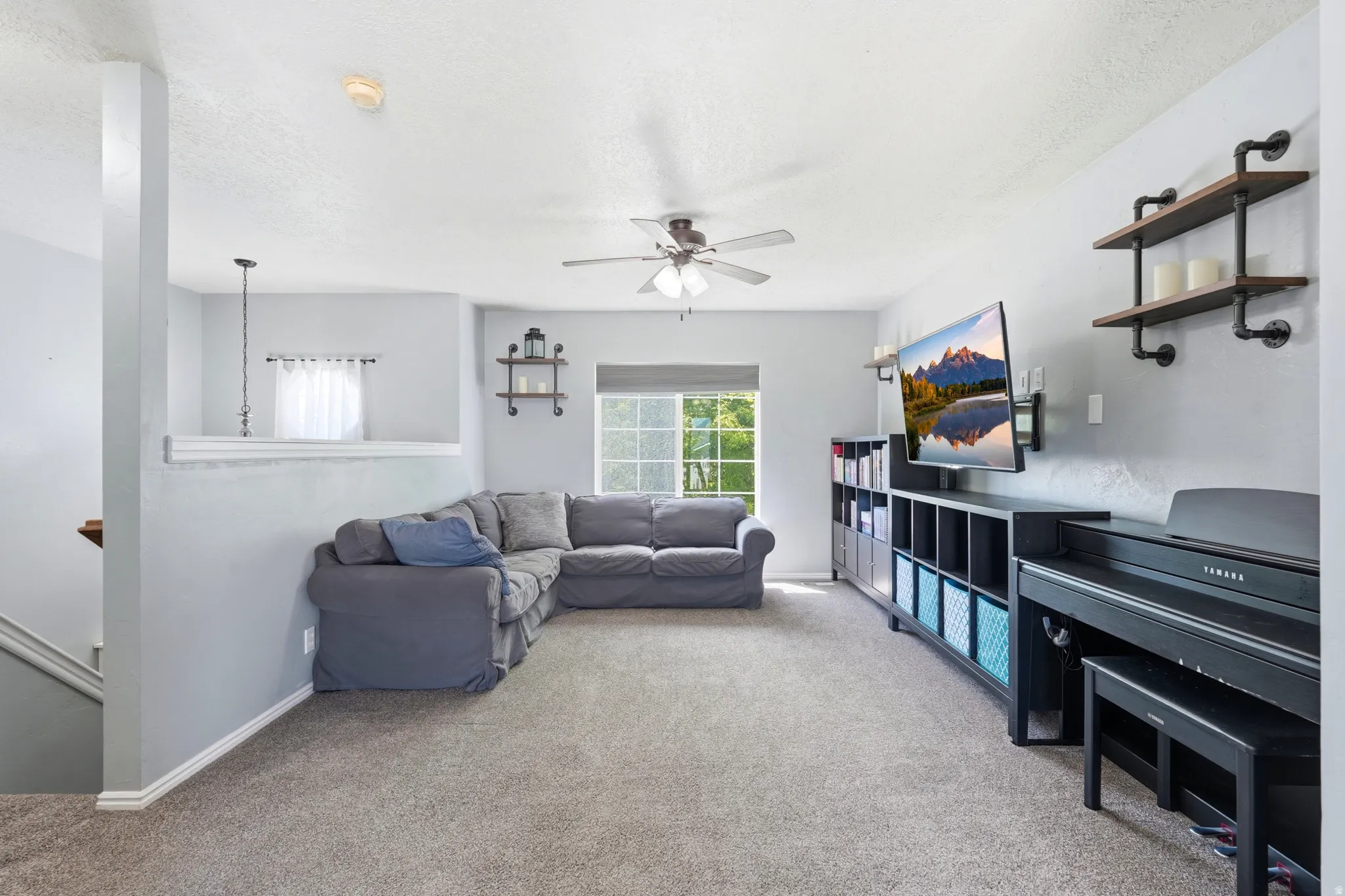 Spacious living area featuring neutral carpeting, a ceiling fan, and a built-in shelving unit