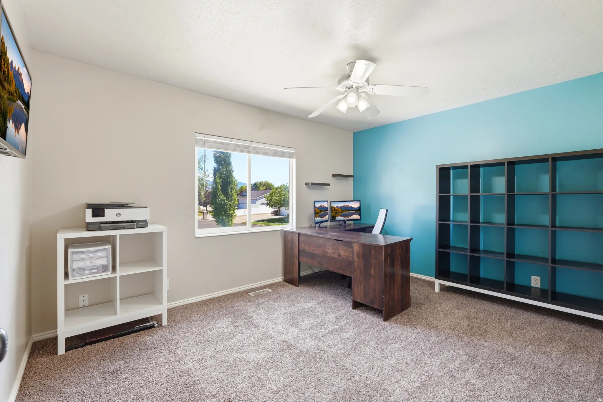 Spacious room featuring carpeting, a prominent window, ceiling fan with light fixture, and a built-in shelving unit