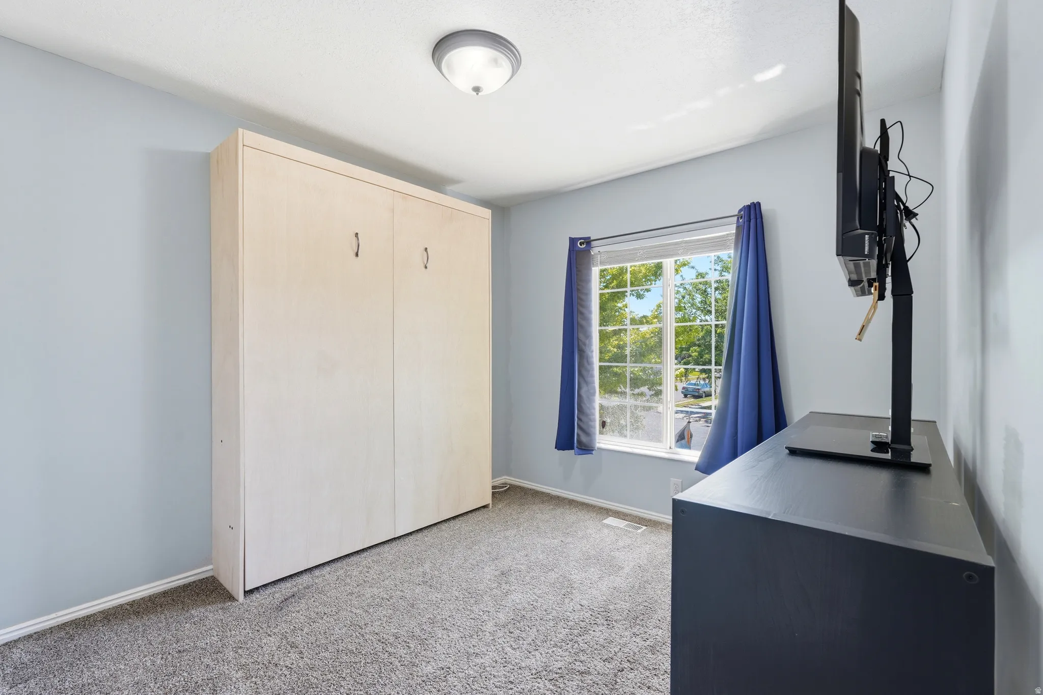 Room featuring a light-toned wood-finish built-in wall unit, a window with exterior visibility, and a gray carpeted floor