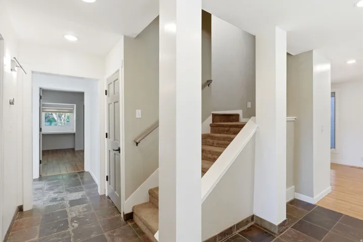 Entryway featuring stone-look tile flooring, recessed lighting, a carpeted staircase with a metal handrail, and a paneled interior door with black hardware