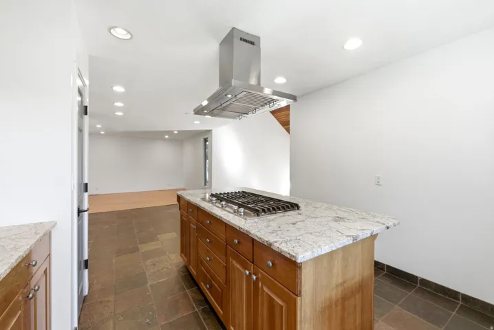 Kitchen island featuring a gas cooktop, granite countertop, wood cabinetry, and stainless steel range hood