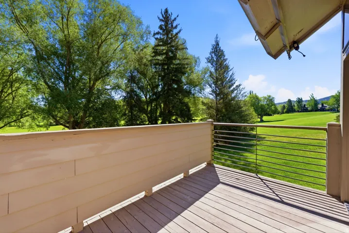 Outdoor deck featuring wood-finish flooring, a horizontal cable railing system, and a scenic green landscape with mature trees