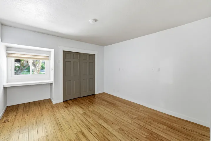 Room featuring wood-finish flooring, a window with a built-in sill and wood blinds, and a closet with paneled bi-fold doors