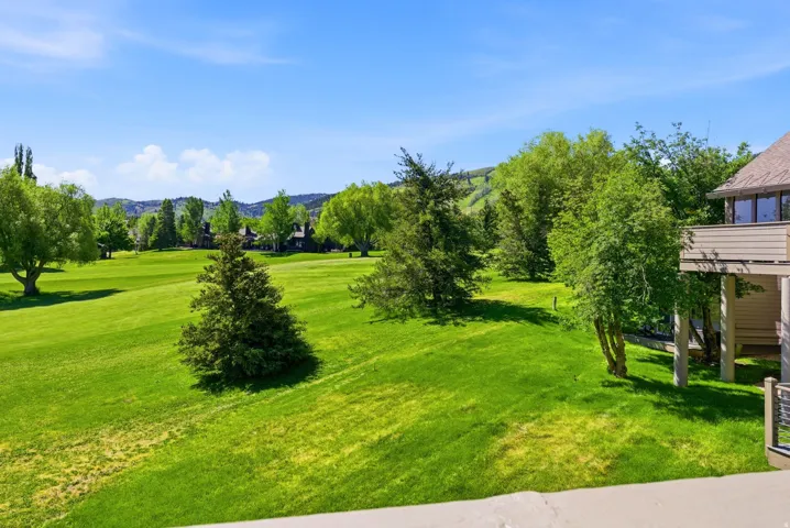 Expansive green lawn with mature trees and distant mountain terrain