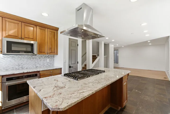 Kitchen island with a built-in gas cooktop, granite countertop, and stainless steel range hood
