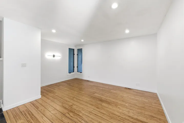 Spacious room featuring wood-finish flooring, recessed lighting, and a modern wall sconce