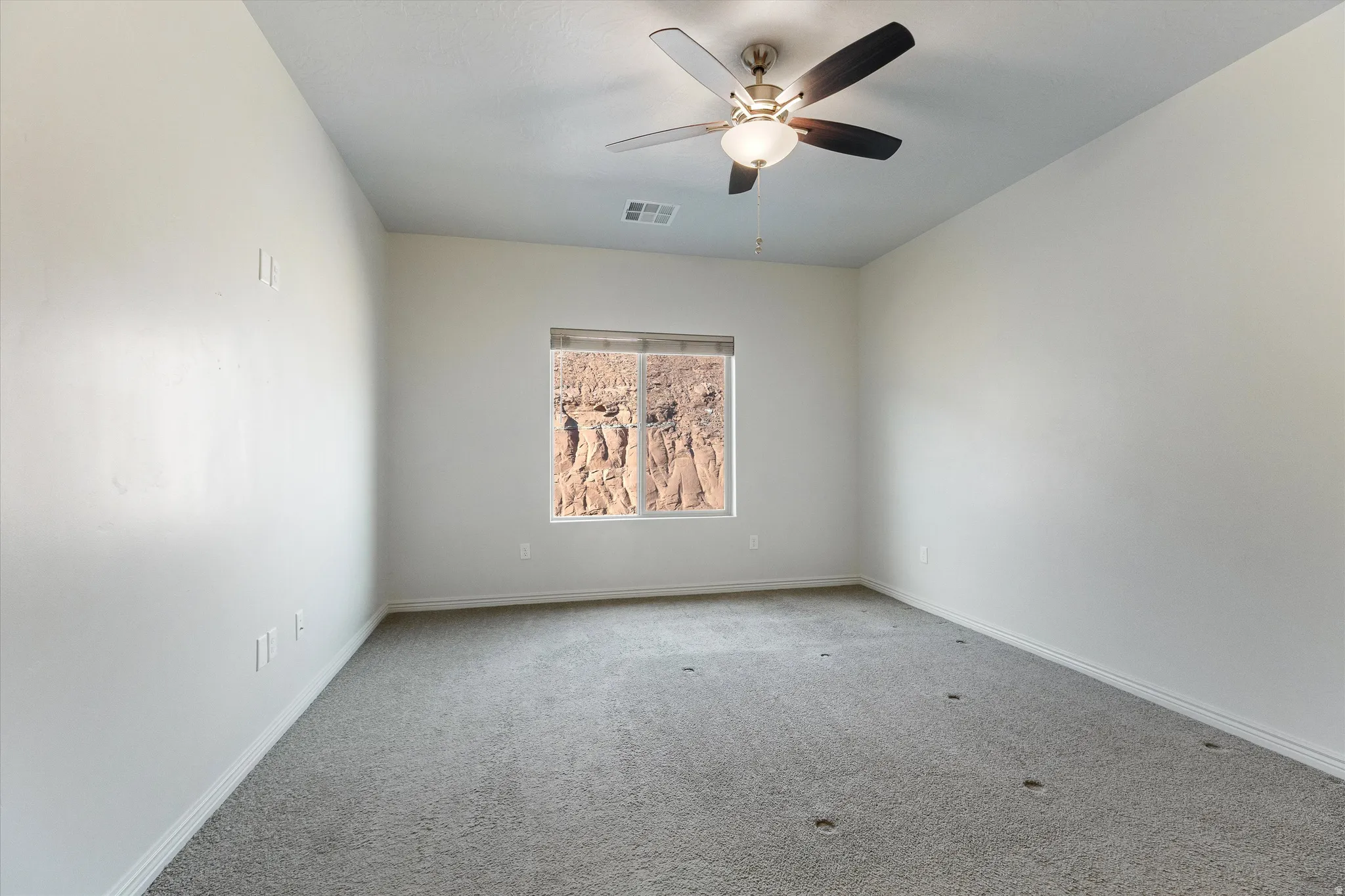 Spacious room featuring neutral carpeting, a ceiling fan with integrated lighting, and a window framing a rock formation landscape