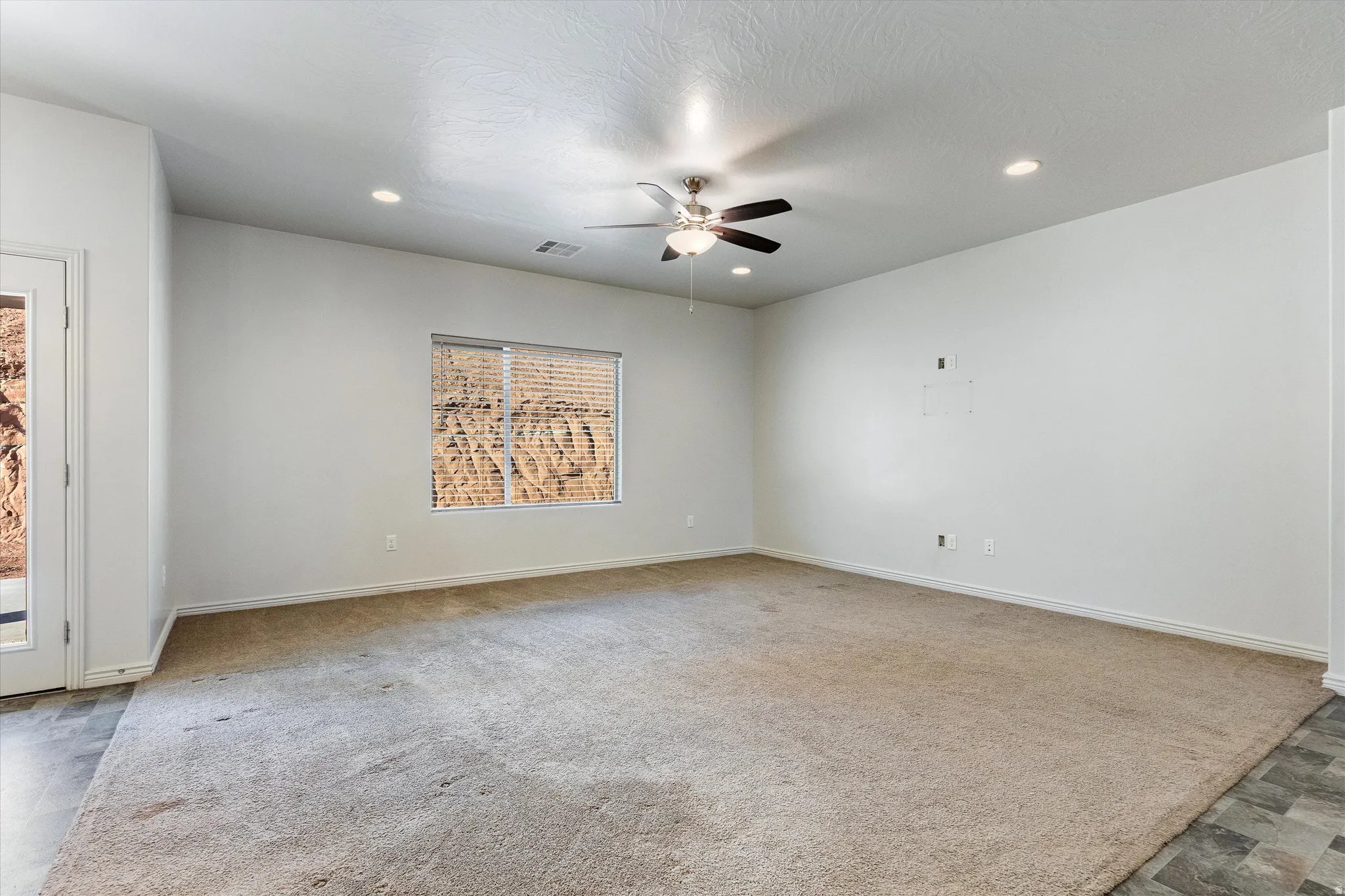 Spacious room featuring neutral carpeting, a ceiling fan, recessed lighting, and a window with blinds