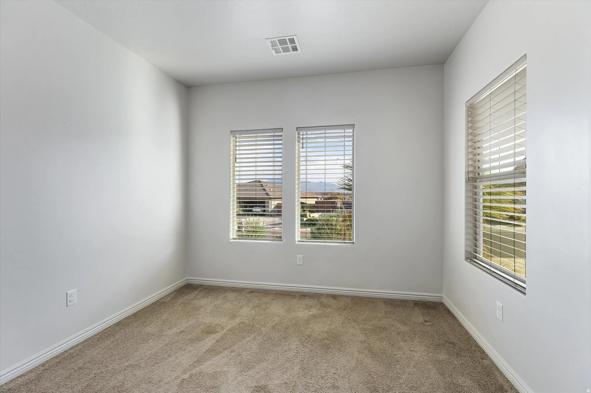 Room featuring carpet flooring, crisp white walls, multiple windows with blinds, and white baseboards