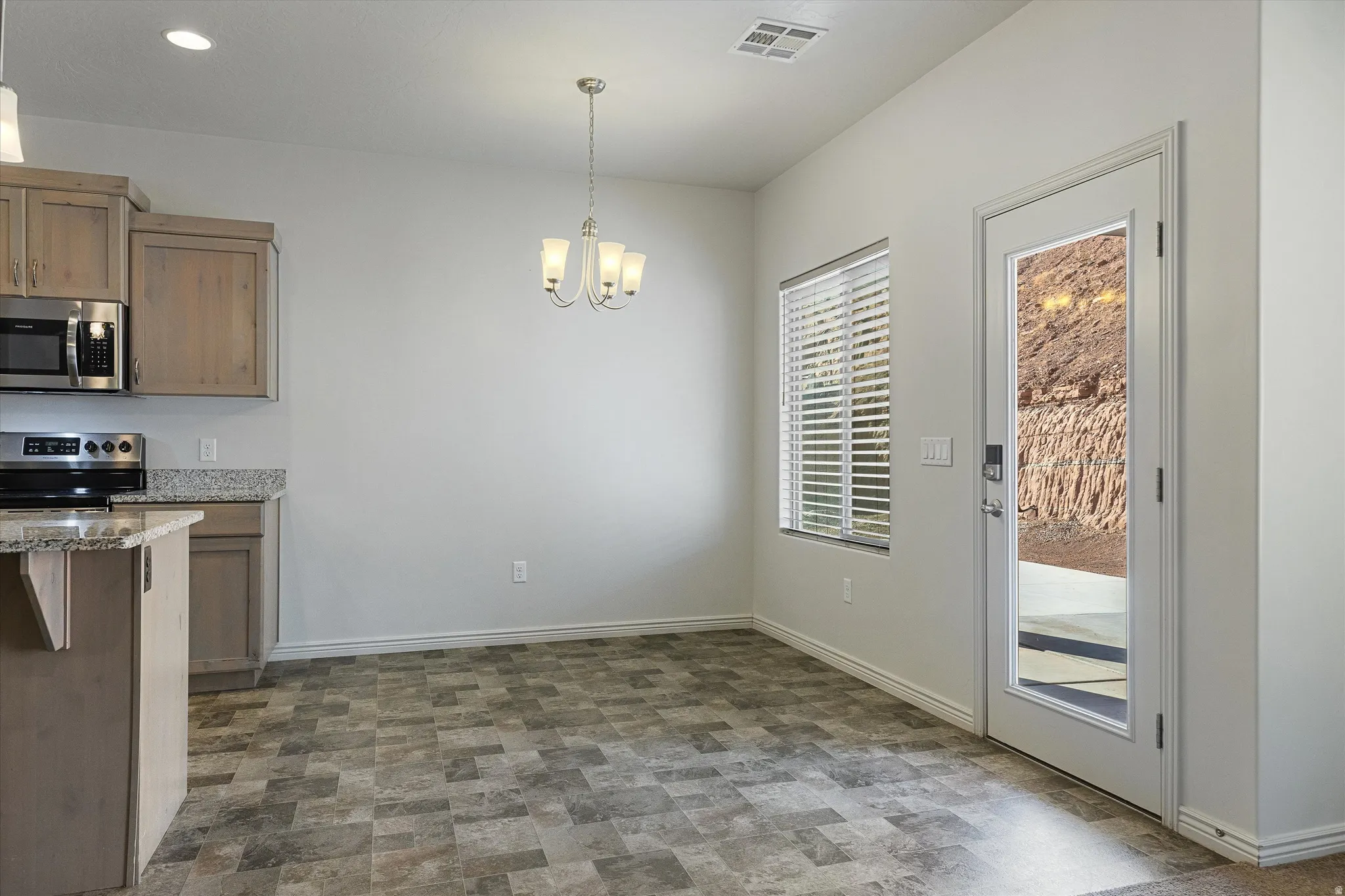 Kitchen and dining area featuring stainless steel appliances, granite-style countertops, wood-finish cabinetry, and a full-light exterior door