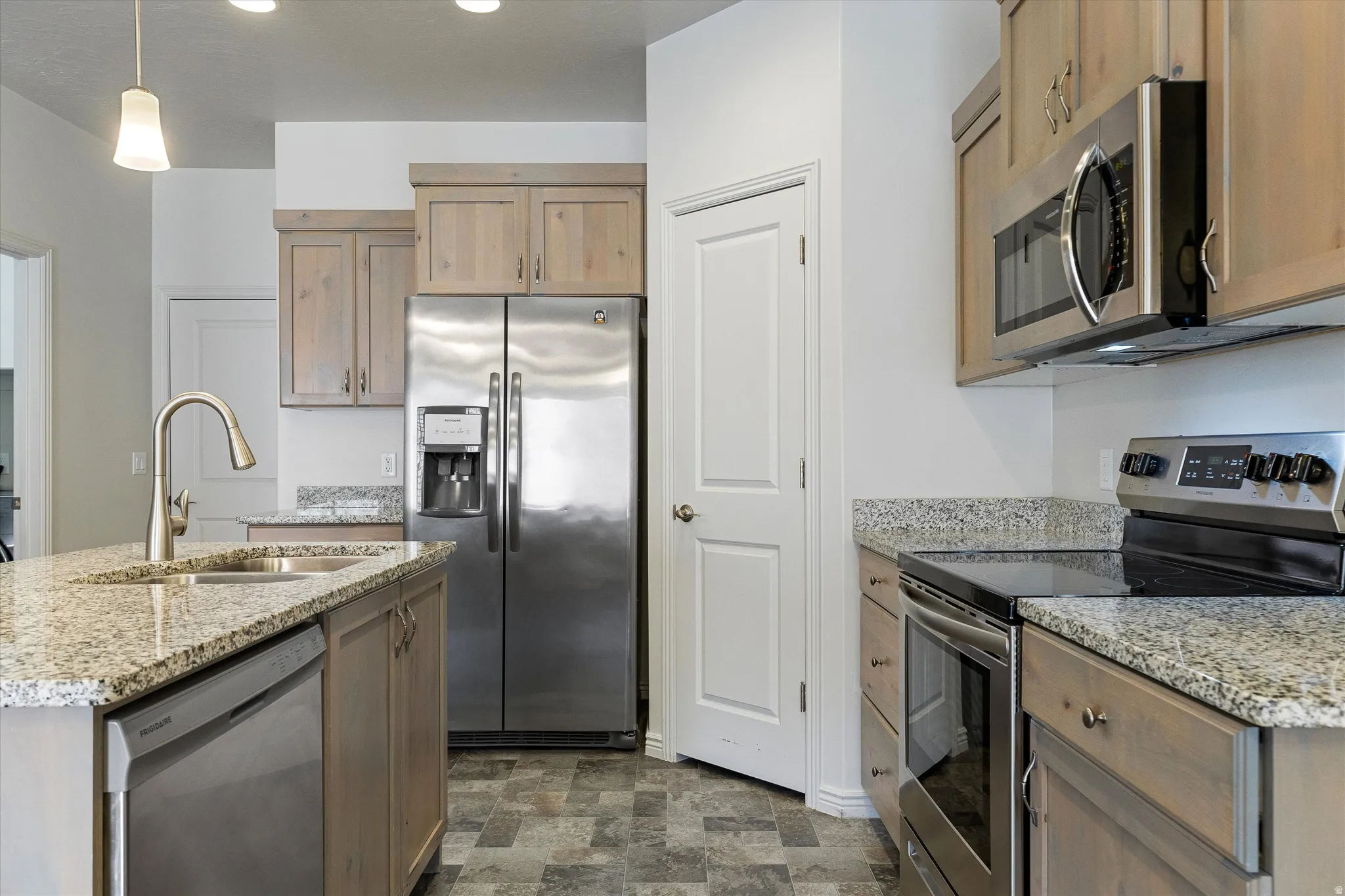 Kitchen featuring stainless steel appliances, light wood-finish cabinetry, granite countertops, and patterned floor tiling
