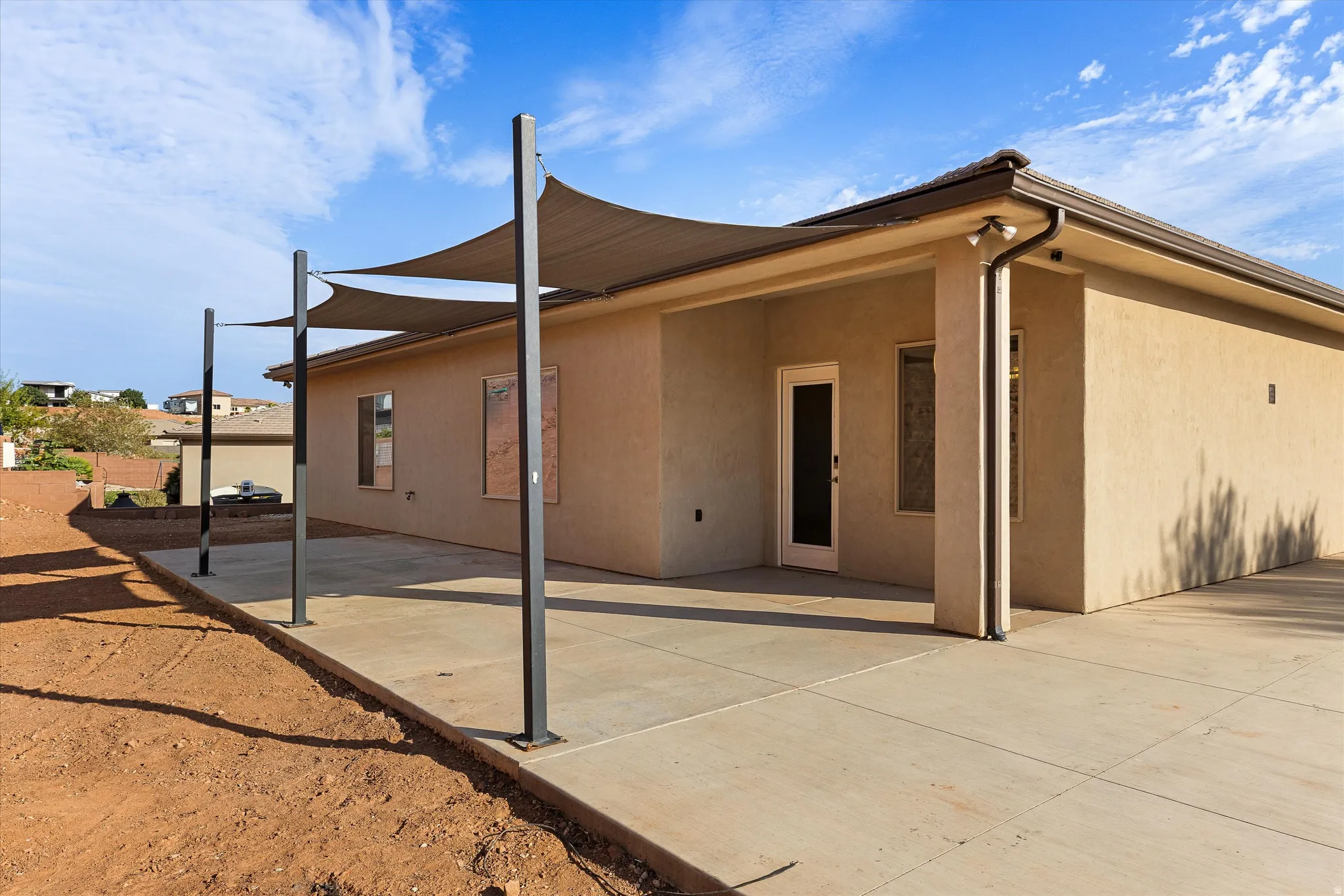 Expansive concrete patio featuring multiple shade sails and a stucco exterior