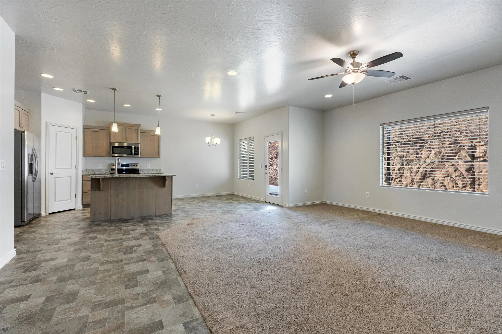 Open-concept living area featuring a kitchen with light wood-finish cabinetry, a stone-finish countertop island, and stainless steel appliances