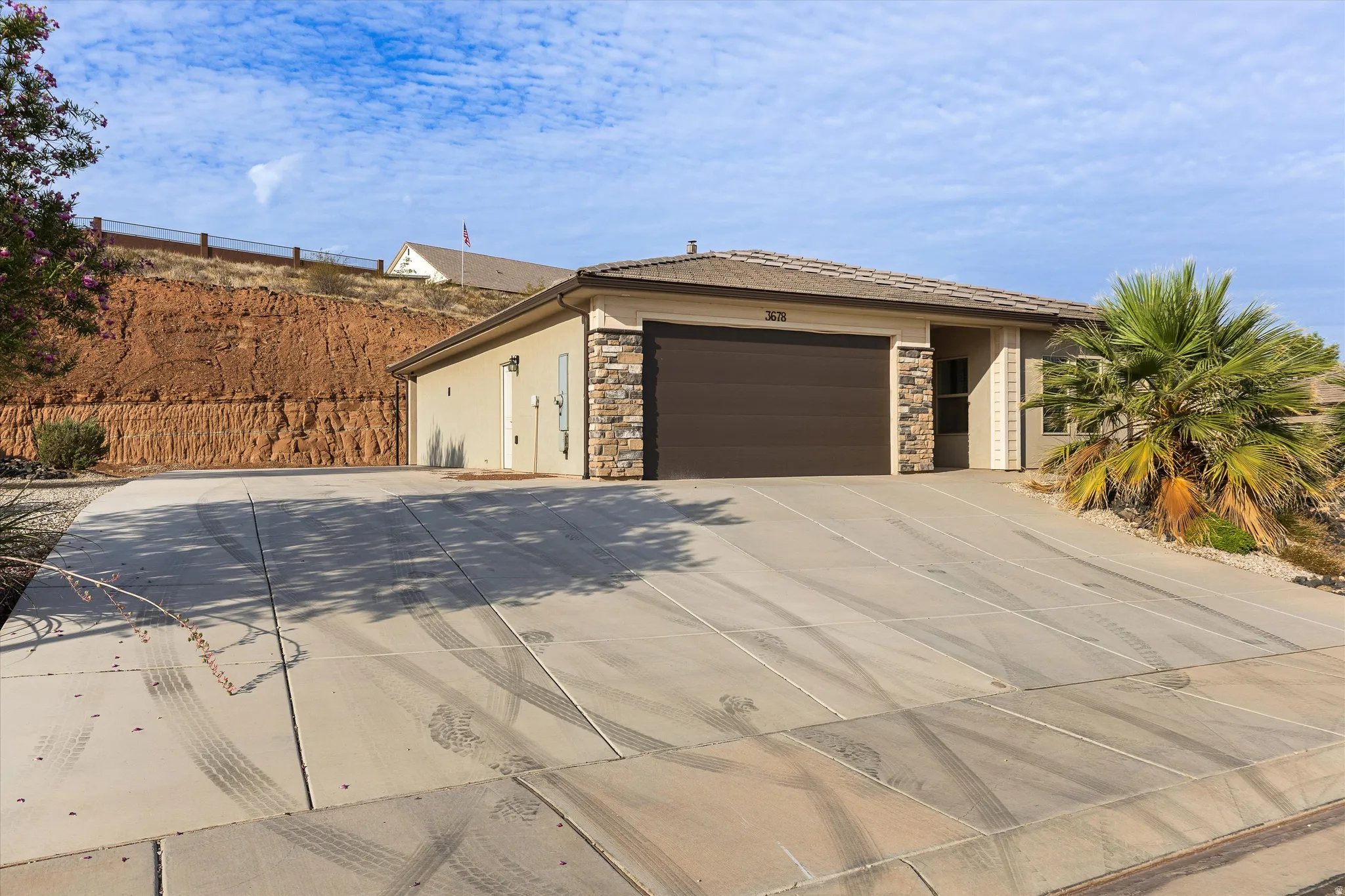 Single-story residence featuring a two-car garage with a brown door, stone veneer accents, stucco exterior, and a tiled roof