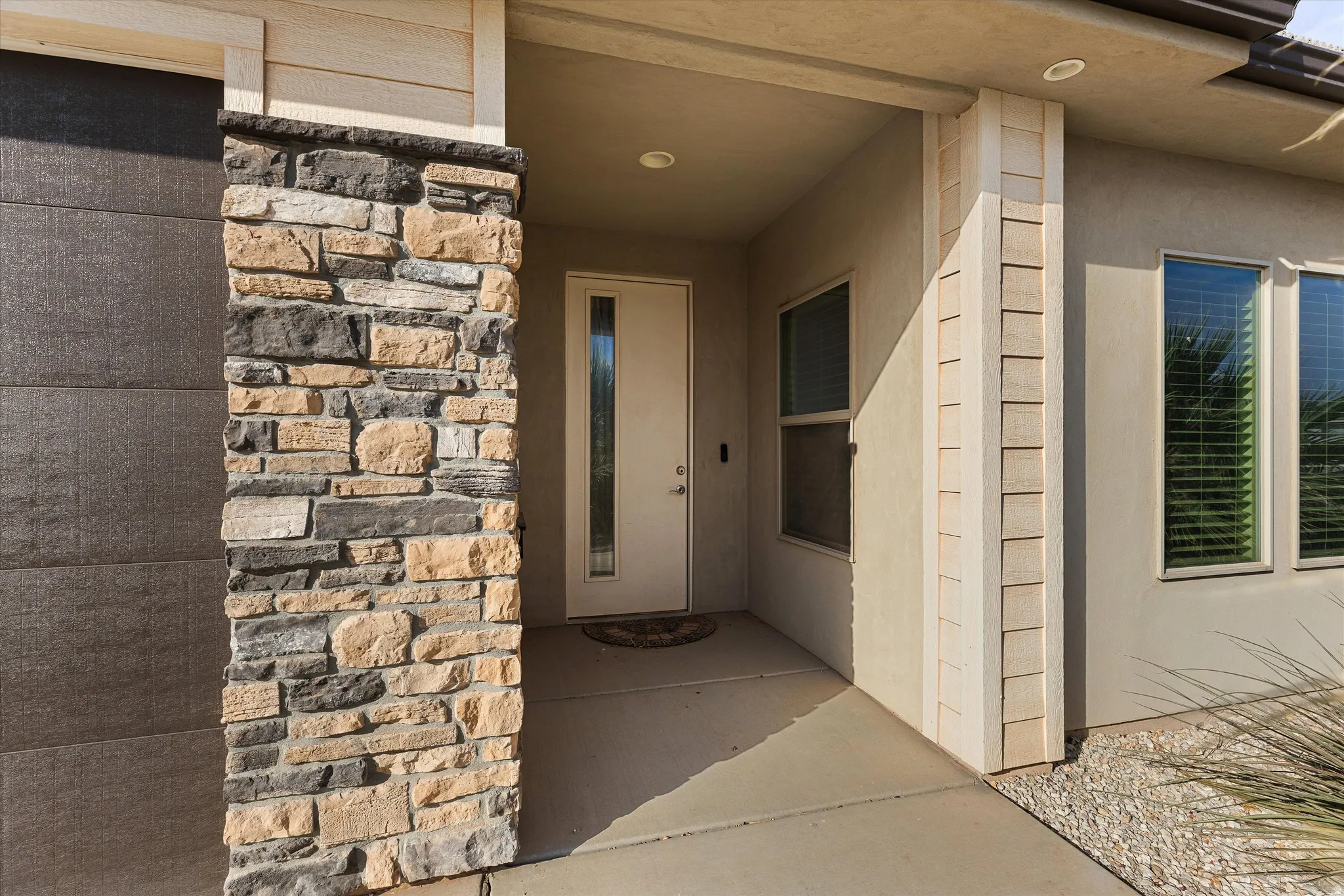 Entryway featuring a stone-clad column, smooth stucco exterior, recessed lighting, and a front door with an elongated glass insert