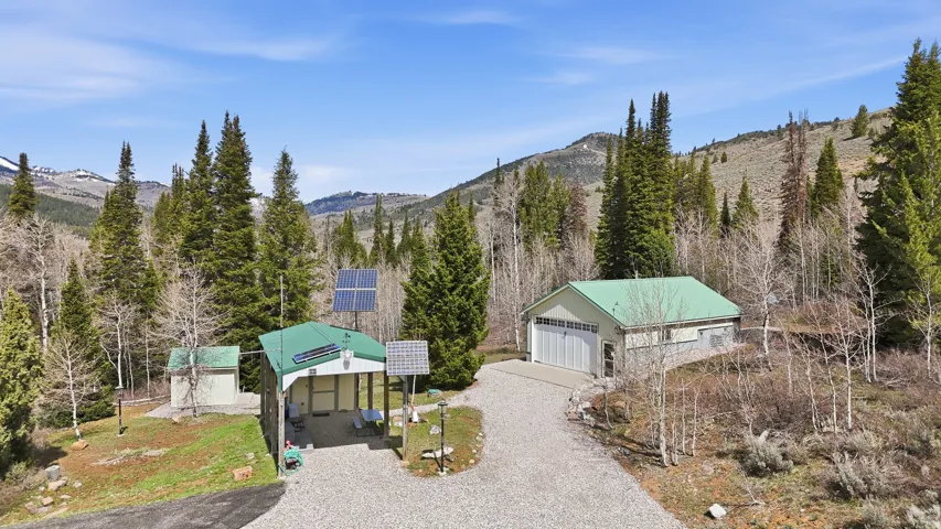Mountain property featuring a detached garage with a green metal roof, a gravel driveway, and a separate structure with multiple solar panels