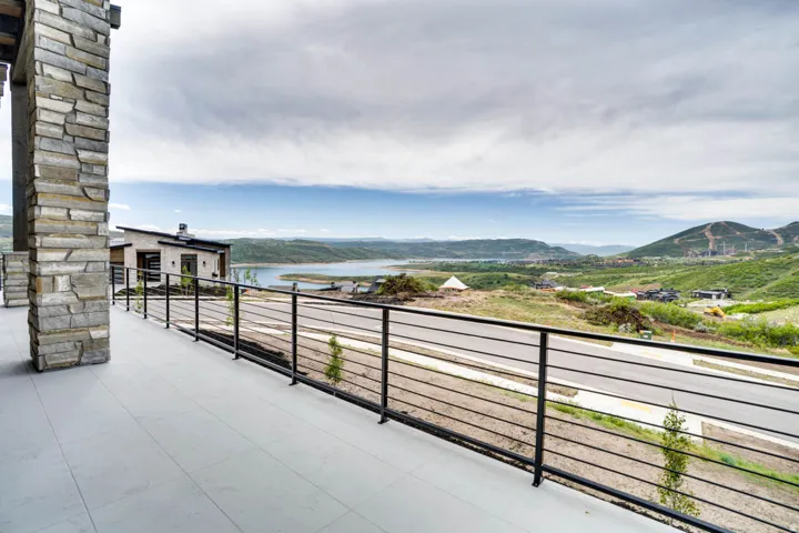 Exterior balcony featuring a stone-clad pillar, horizontal metal railing, and light-toned flooring