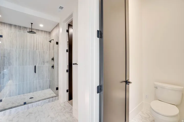 Spacious bathroom featuring a glass-enclosed shower with full-height tile surround, a ceiling-mounted rainfall showerhead, a wall-mounted showerhead, and matte black fixtures