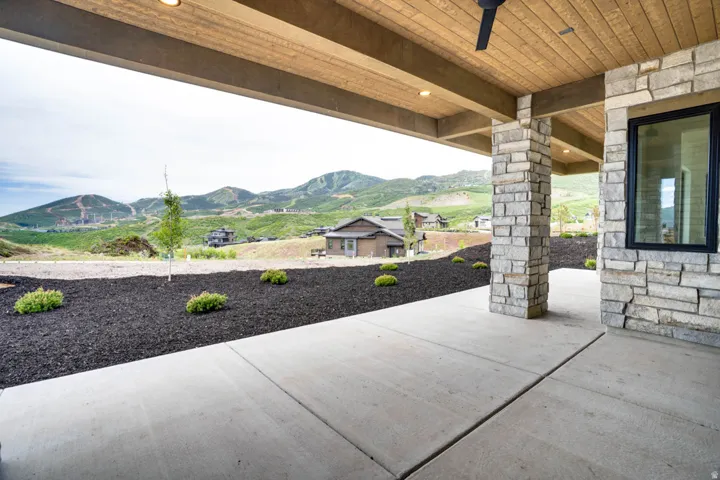 Covered patio with a concrete surface, stone-clad columns, and a wood-finish ceiling with recessed lighting